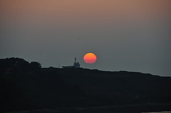 Silhouette of lighthouse at sunset with orange sun