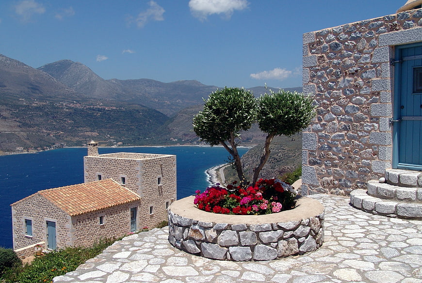 Traditional Greek stone house terrace with olive trees and coastal mountain view