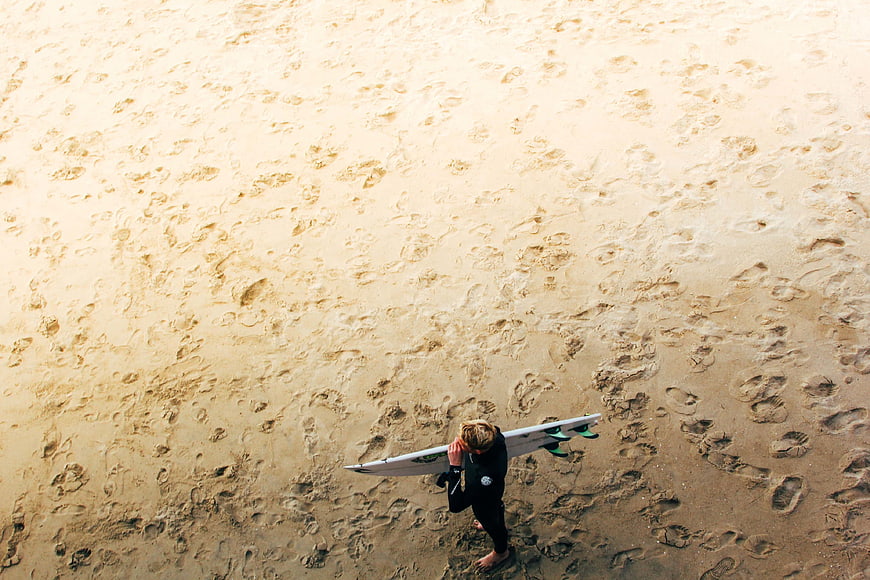 Aerial view of surfer walking on sandy beach with surfboard