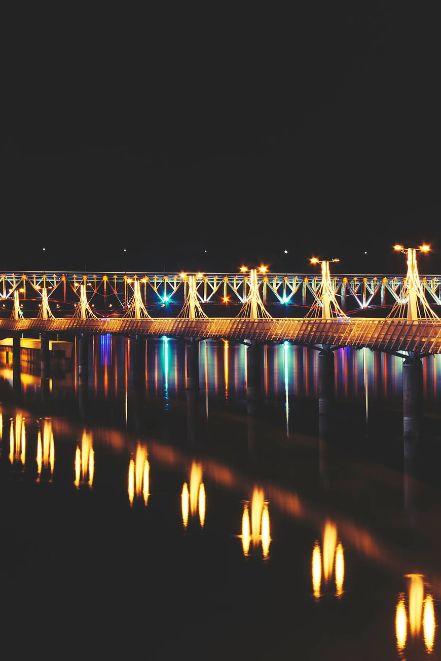 Illuminated pier at night with colorful reflections on water