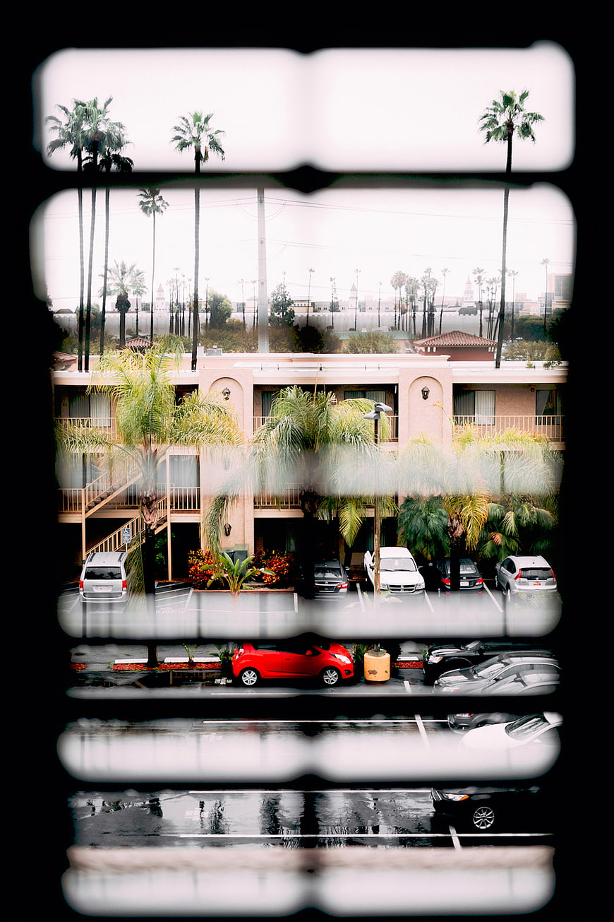 Rainy motel view through window with palm trees and cars