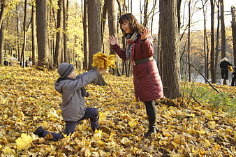 Mother and son playing with autumn leaves in a golden forest