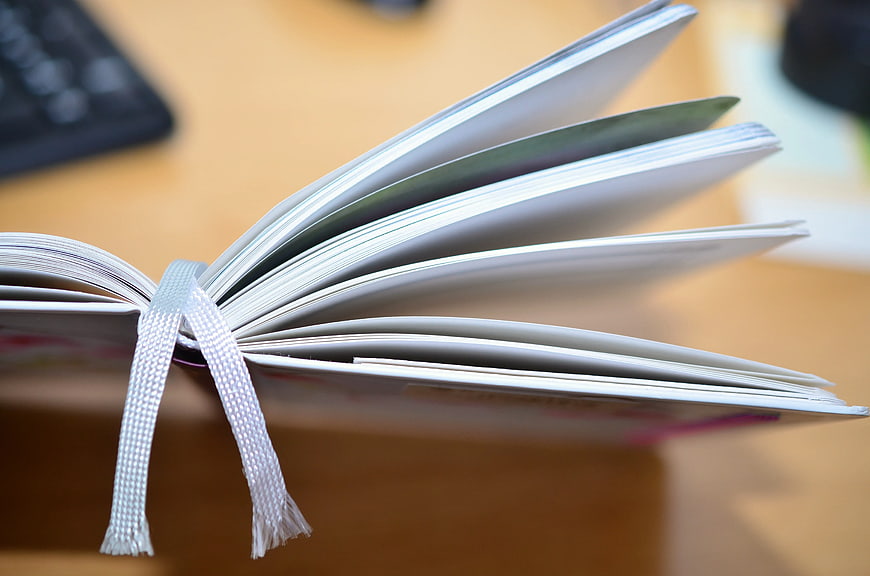 Close-up of open book with white ribbon bookmark on desk