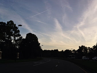 Curved Road at Dusk with Contrails and Silhouetted Trees