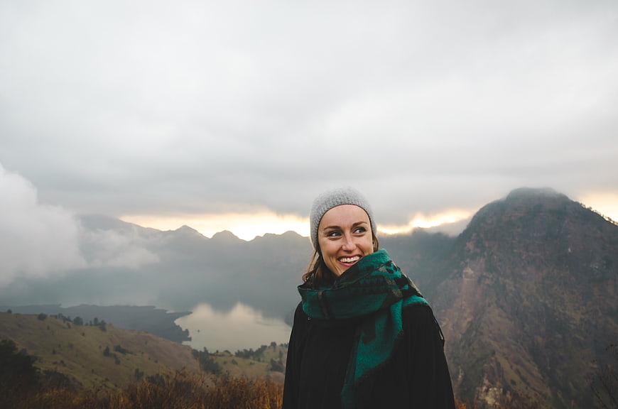 Happy woman in beanie and scarf smiling against misty mountain landscape
