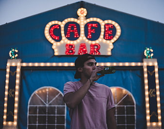Man drinking beer in front of illuminated cafe bar sign
