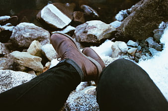 POV of brown leather boots resting on snowy rocks
