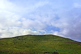 Green rolling hill under cloudy blue sky landscape