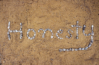 Honesty word spelled with small stones on sandy ground