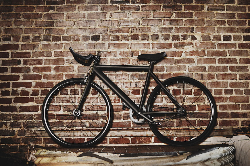 Matte black fixed gear bicycle against rustic brick wall
