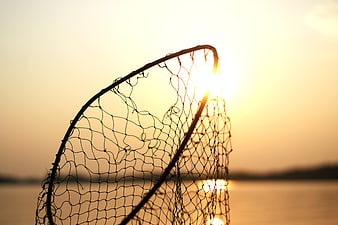 Silhouette of Fishing Net Against Golden Sunset Over Water