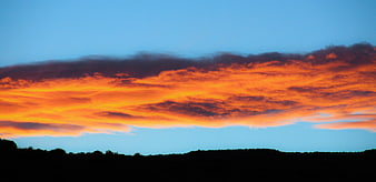 Vibrant orange sunset clouds over dark silhouette landscape