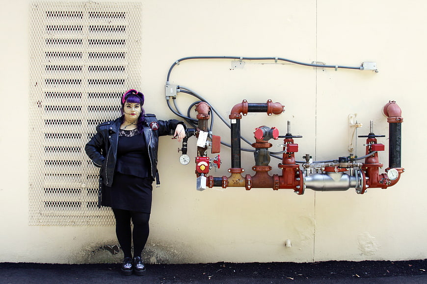 Woman in Gothic Costume Standing by Industrial Pipes
