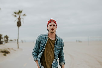 Man in denim jacket and red cap walking on beach