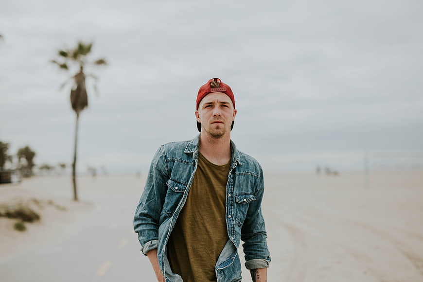 Man in denim jacket and red cap walking on beach