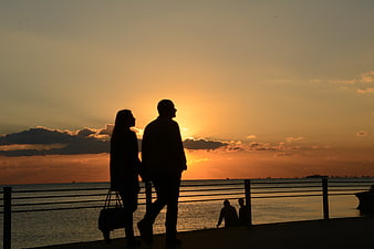 Silhouette of couple walking by sea at sunset