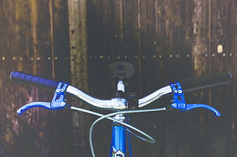 Close-up of blue bicycle handlebars against wooden fence