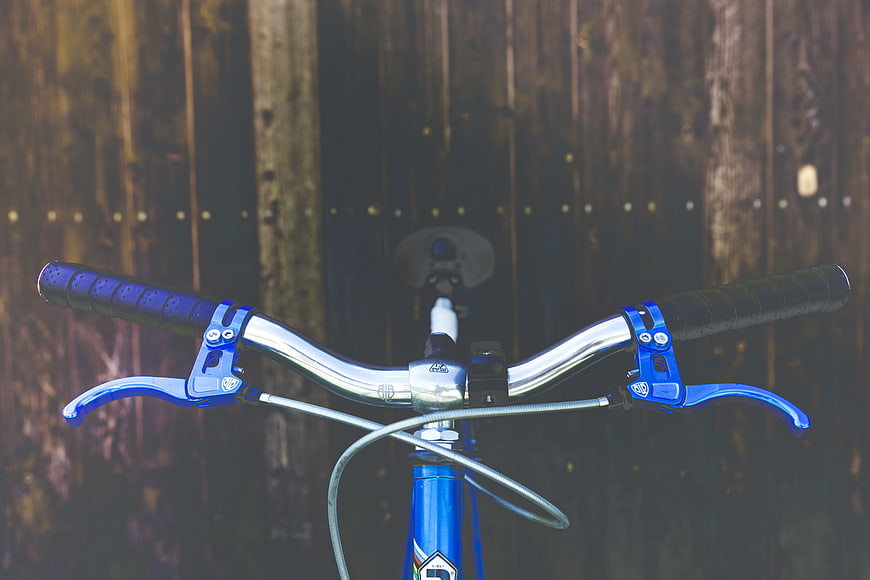 Close-up of blue bicycle handlebars against wooden fence