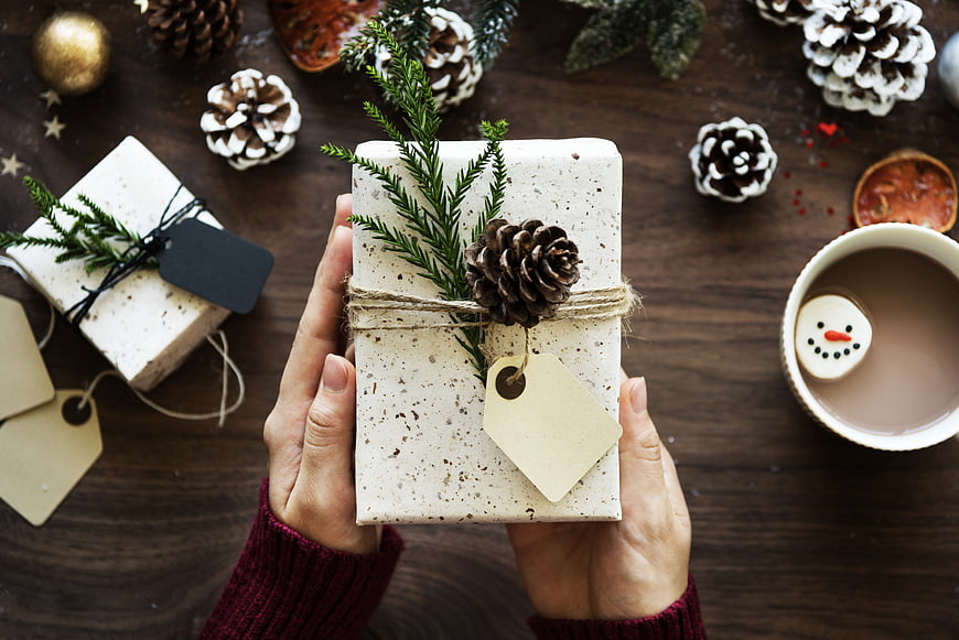 Hands holding rustic Christmas gift with pinecone and hot cocoa