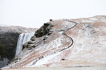 Snowy Skógafoss Waterfall with Winding Staircase and Hikers