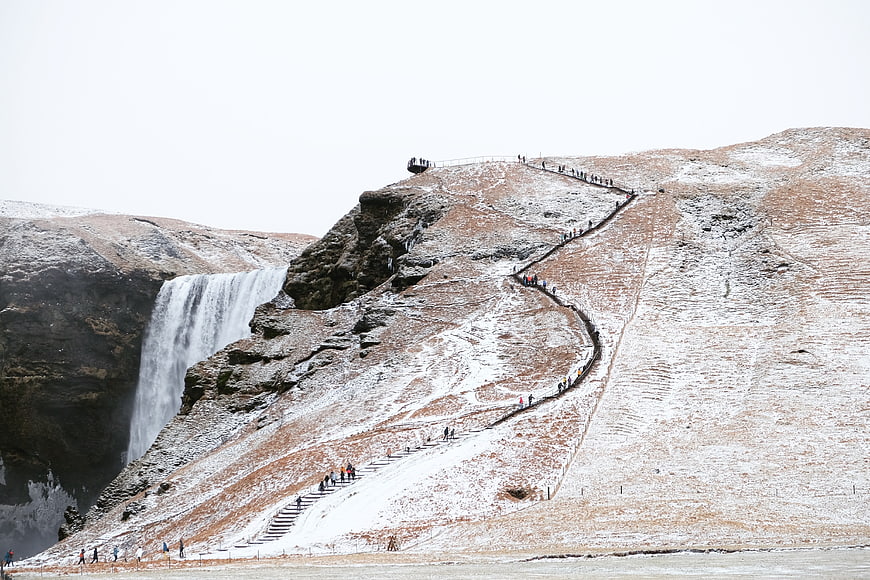 Snowy Skógafoss Waterfall with Winding Staircase and Hikers
