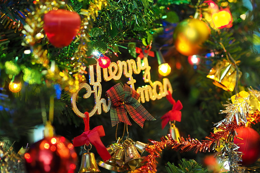 Merry Christmas Ornament On Decorated Tree With Bells And Lights