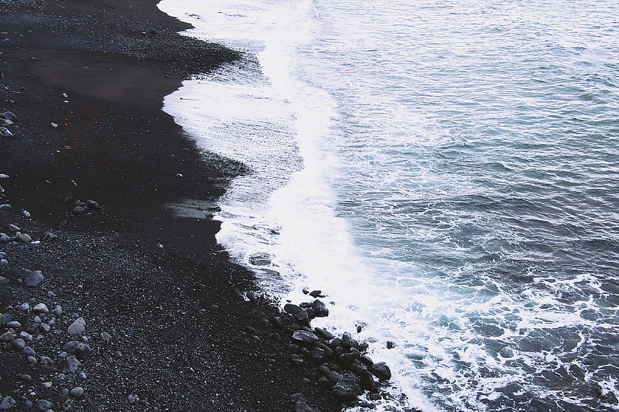 Aerial view of black sand beach with crashing ocean waves