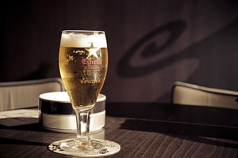 Glass of Estrella Damm beer on a dark wooden table
