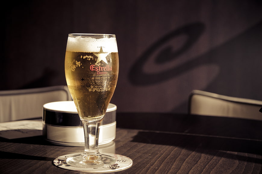 Glass of Estrella Damm beer on a dark wooden table