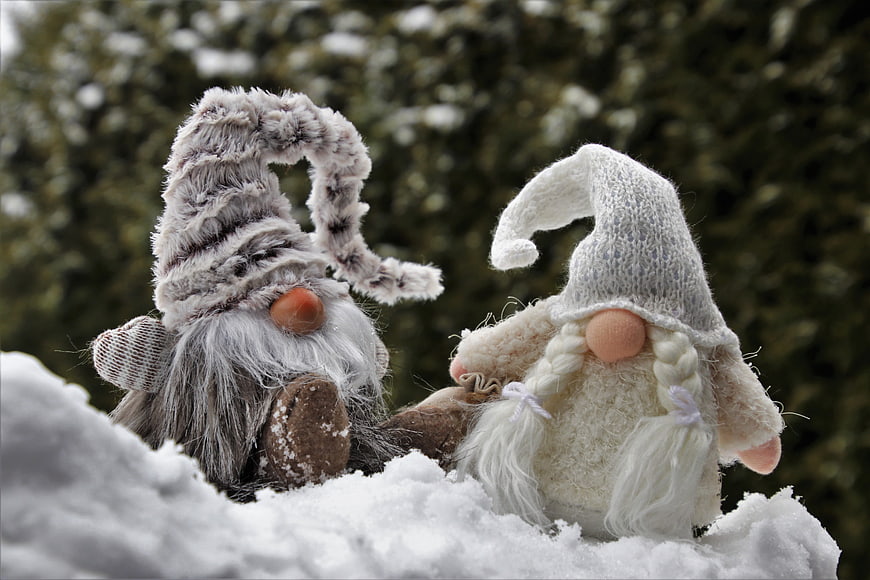 Two Knitted Gnome Figurines Sitting Together In Snow