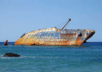 Rusty shipwreck listing in turquoise ocean water under clear blue sky