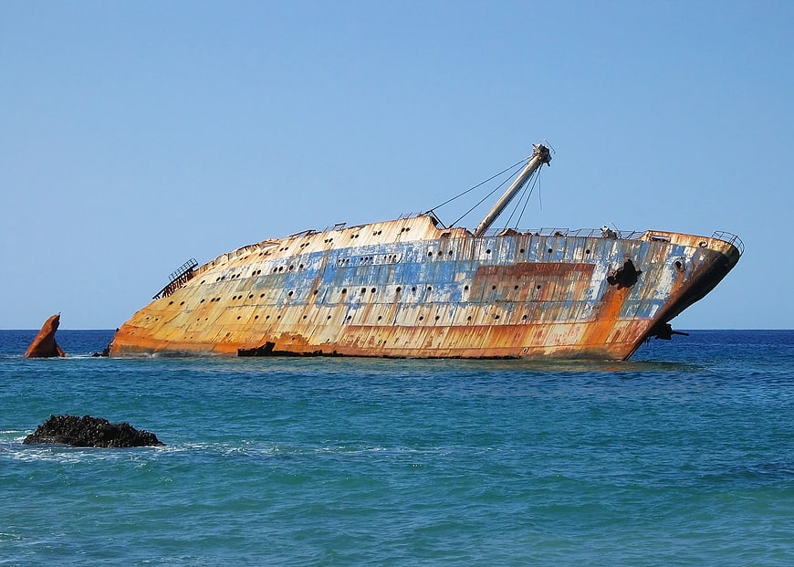 Rusty shipwreck listing in turquoise ocean water under clear blue sky