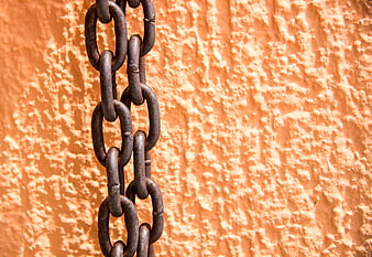 Rusty metal chain hanging against textured orange wall background