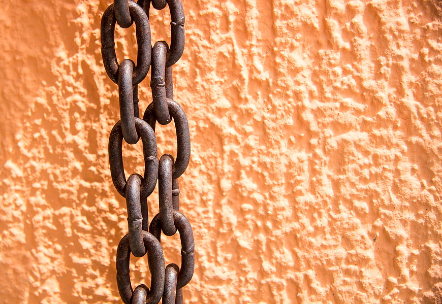 Rusty metal chain hanging against textured orange wall background