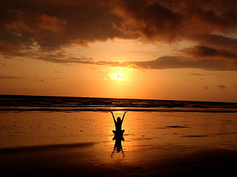 Silhouette of woman meditating on beach at sunset