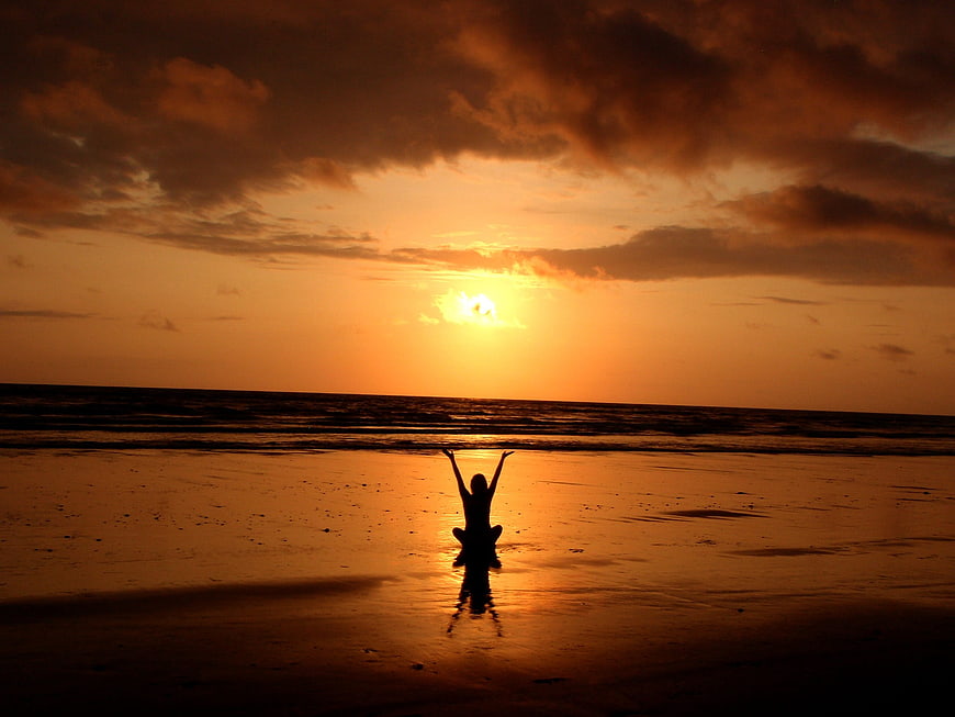 Silhouette of woman meditating on beach at sunset