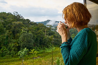 Woman drinking coffee on balcony overlooking lush green mountains