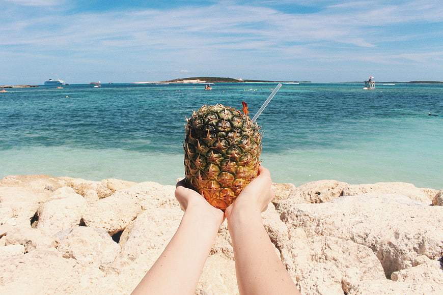 Hands holding pineapple juice drink on tropical beach