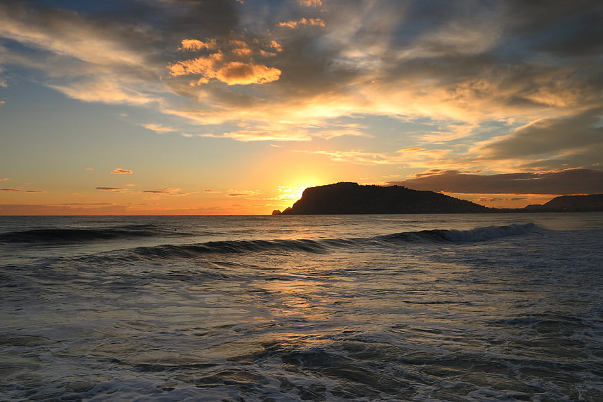 Golden Sunset Over Ocean Waves and Silhouette Cliff