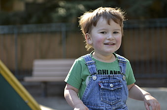 Smiling young boy in denim overalls and green t-shirt outdoors