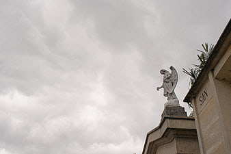 Stone Angel Statue on Cemetery Tomb Against Cloudy Sky