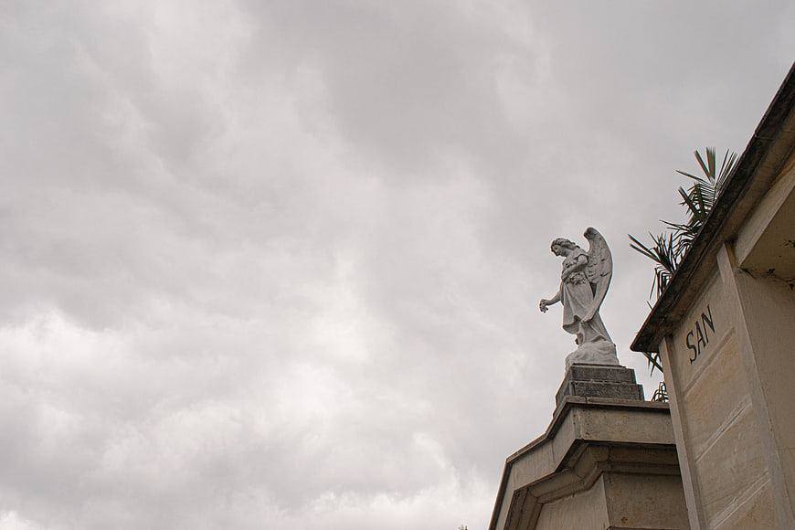 Stone Angel Statue on Cemetery Tomb Against Cloudy Sky