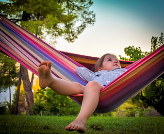 Young girl relaxing in a colorful striped hammock outdoors
