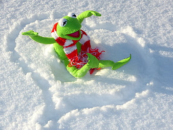 Green frog puppet wearing red scarf in snow