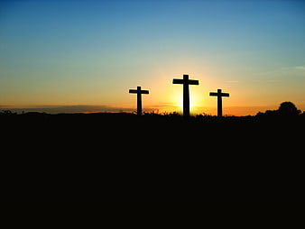Silhouette of three crosses on a hill against a sunset sky