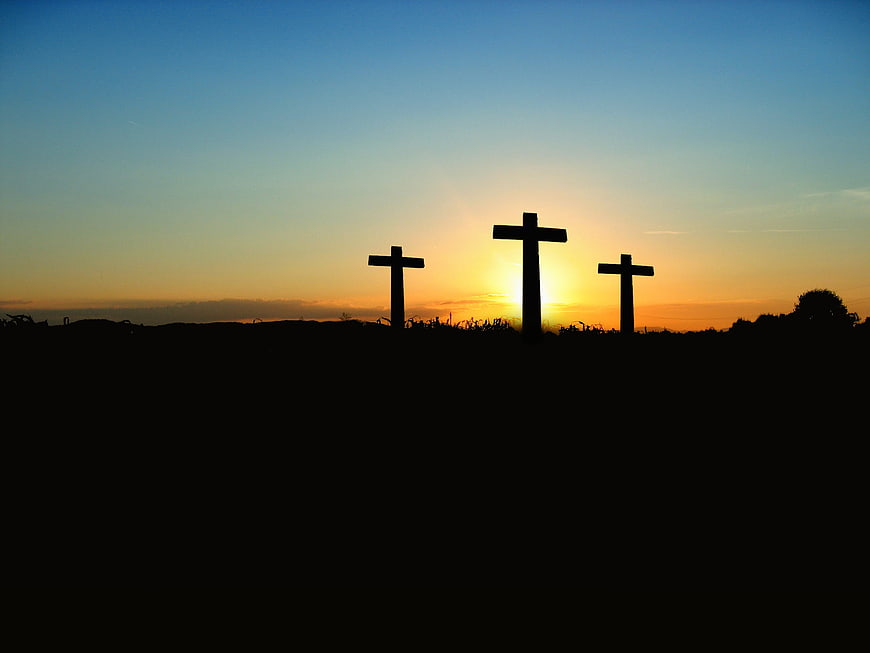 Silhouette of three crosses on a hill against a sunset sky