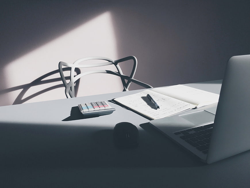 Minimalist workspace with laptop, notebook, and calculator in sunlight