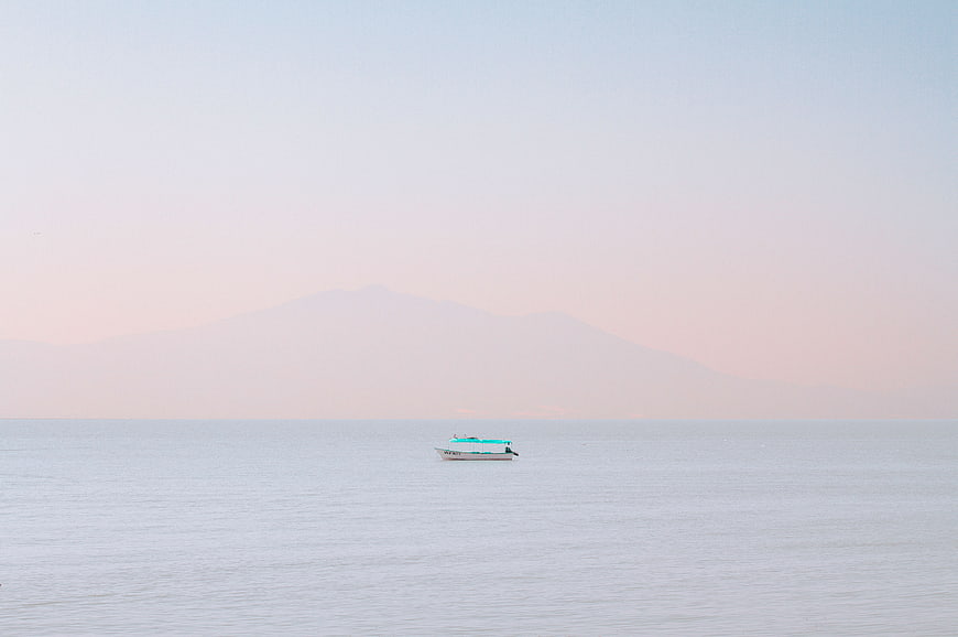 Minimalist boat on calm sea with distant mountain silhouette