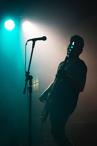 Silhouette of male guitarist performing on stage with teal lights