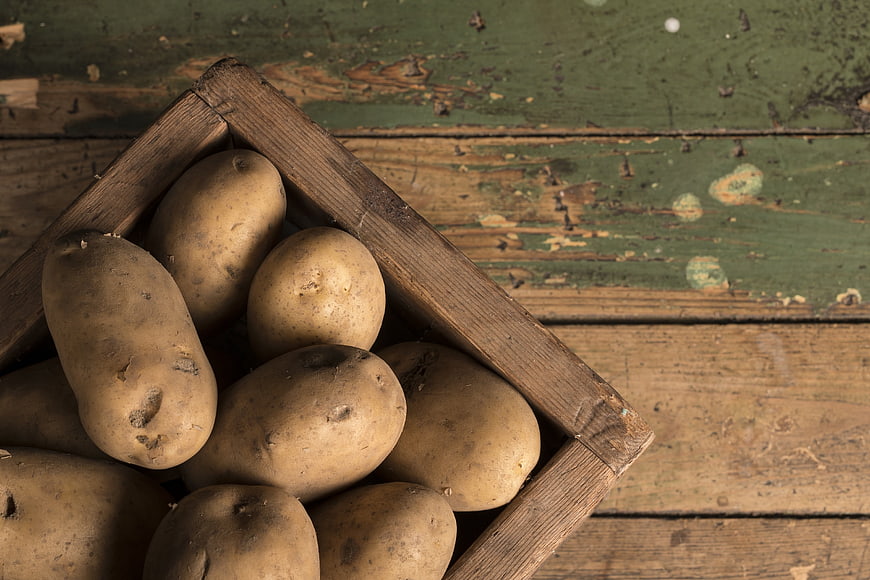 Fresh raw potatoes in rustic wooden crate on vintage table
